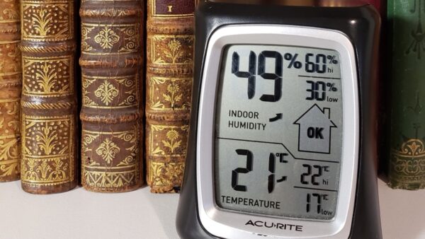 A digital hygrometer with books behind it.